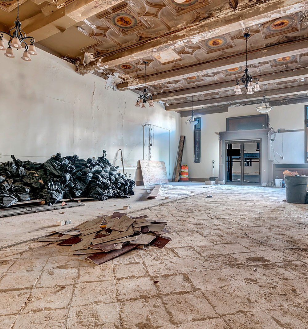 Interior under construction with an ornate patterned ceiling, exposed beams, and debris across the floor.