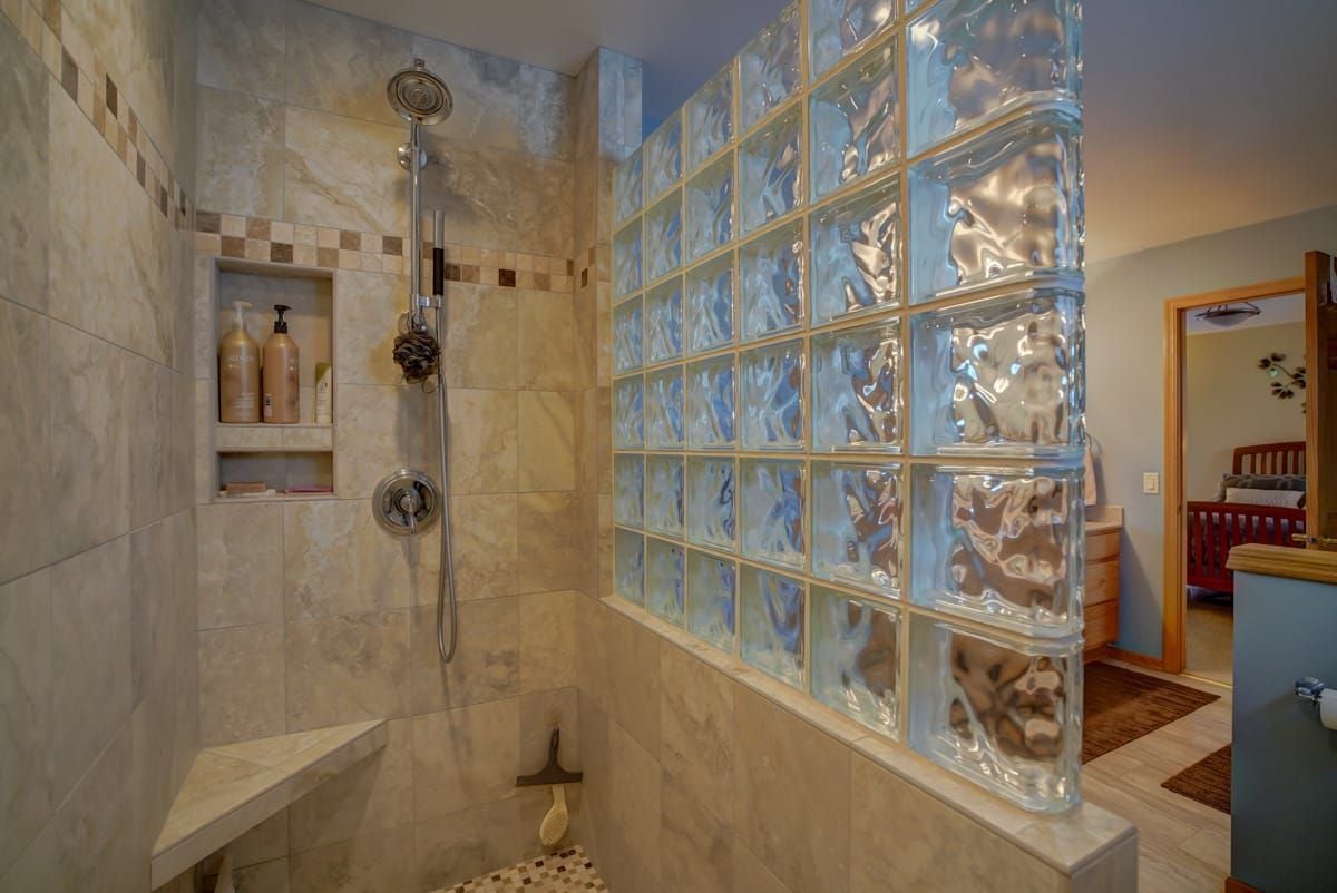 Walk-in shower with beige tile, a built-in bench, recessed shelves, and a glass-block partition.