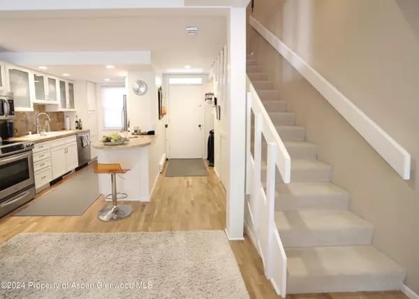 Open kitchen and entry with white cabinets, a small island, and a carpeted staircase.