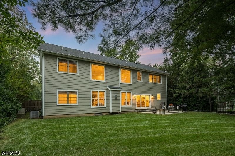 Two-story gray house with glowing windows, a broad lawn, and patio seating at dusk.