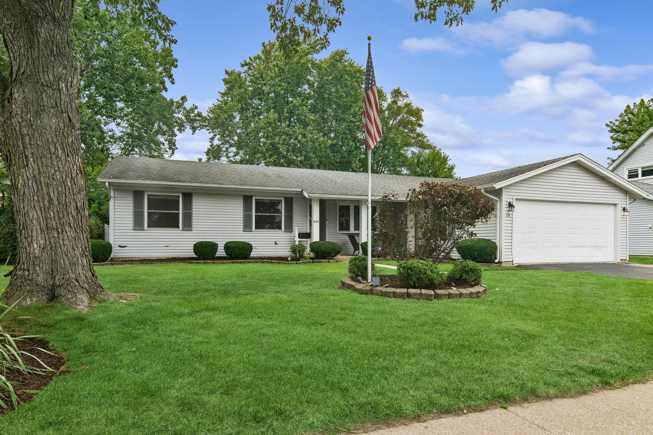 Single-story white house with an attached garage, green lawn, and American flag.