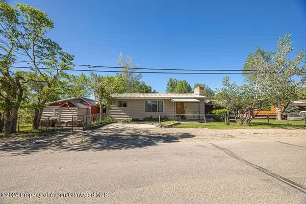 Single-story ranch home with tan siding, a covered front porch, and mature trees.