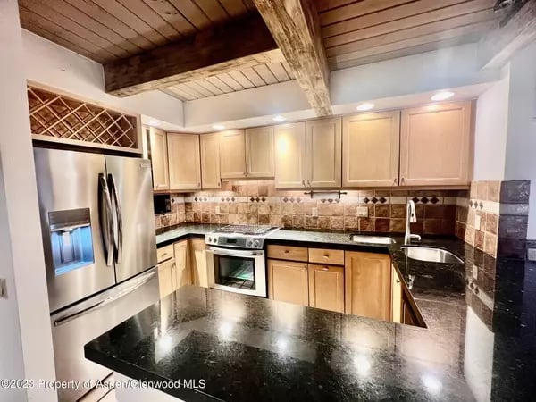 Kitchen with black stone counters, stainless steel appliances, and a vaulted wood ceiling with exposed beams.