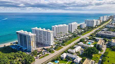 Aerial view of beachfront high-rises beside turquoise water and a coastal road.