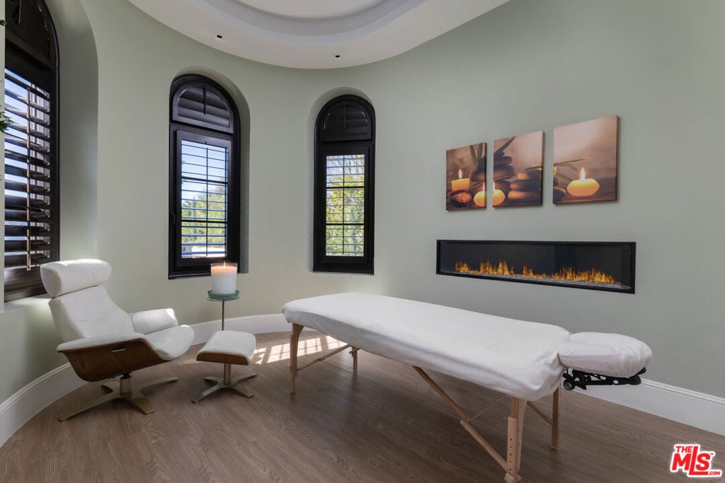 Massage room with a massage table, lounge chair, arched windows, and linear fireplace.