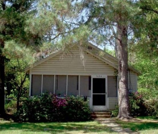 A small house with a porch surrounded by trees in a well-maintained yard.