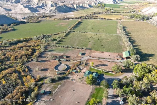 Aerial view of a rural property with fields, farm buildings, and rugged mountains beyond.