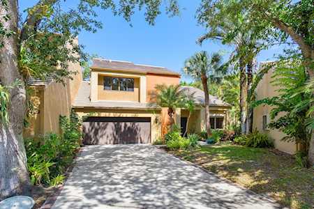 Two-story tan stucco home with a double garage and landscaped front yard beneath mature trees.