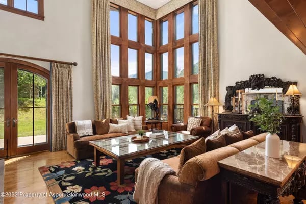 Living room with towering wood-framed windows, brown sofas, and a glass coffee table.