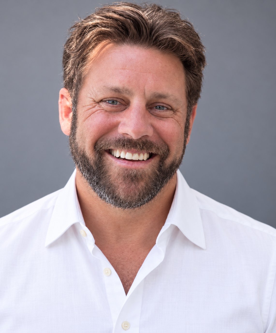 Smiling bearded man in a white shirt against a gray background.