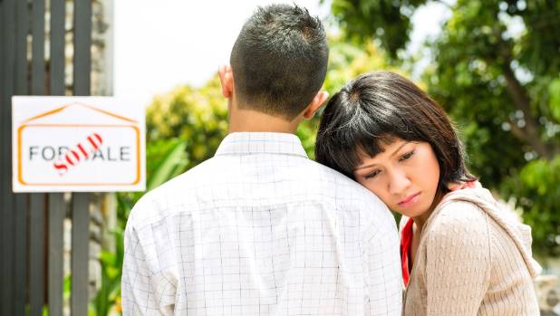 A worried woman leans against a man beside a for-sale sign stamped SOLD.