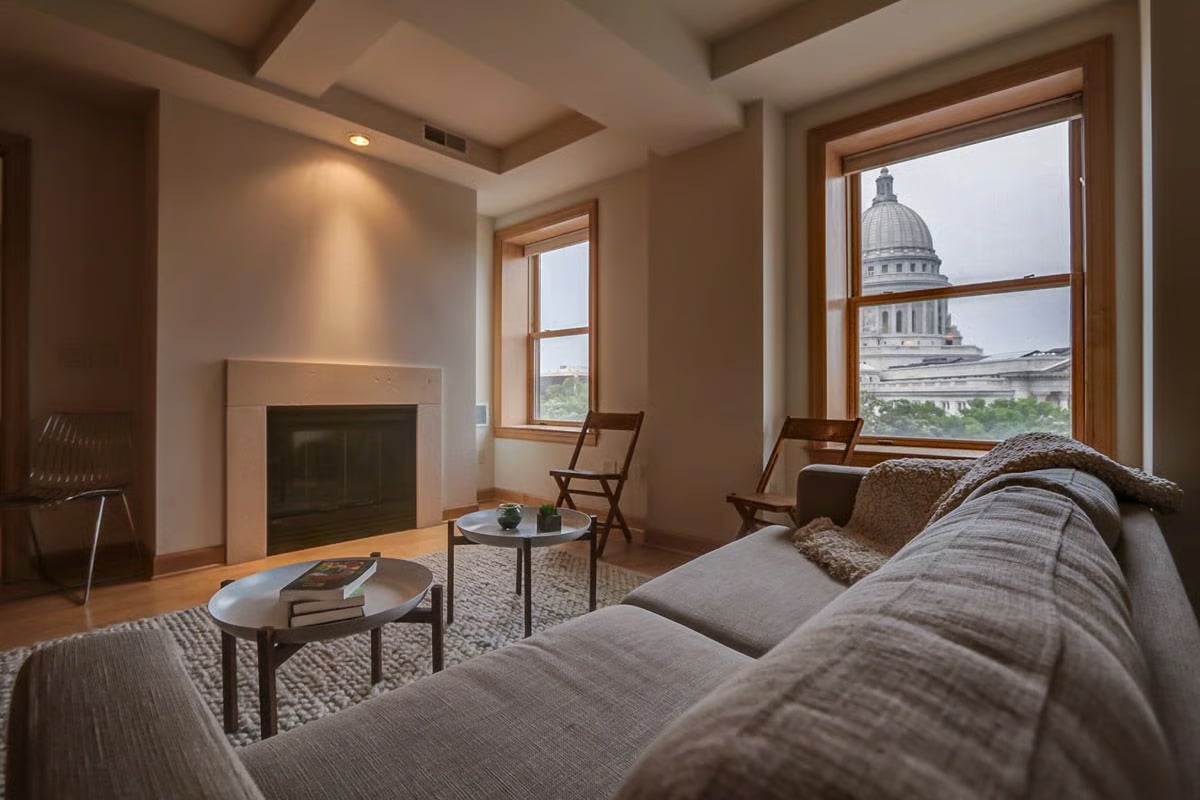 Living room with a fireplace and gray sectional, overlooking the capitol through tall windows.