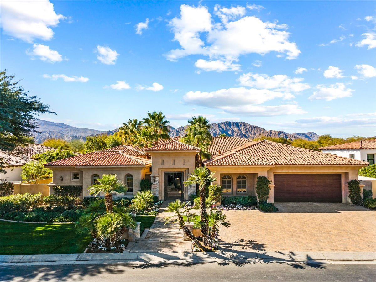 Single-story stucco home with a tiled roof, landscaped yard, and mountains in the background.