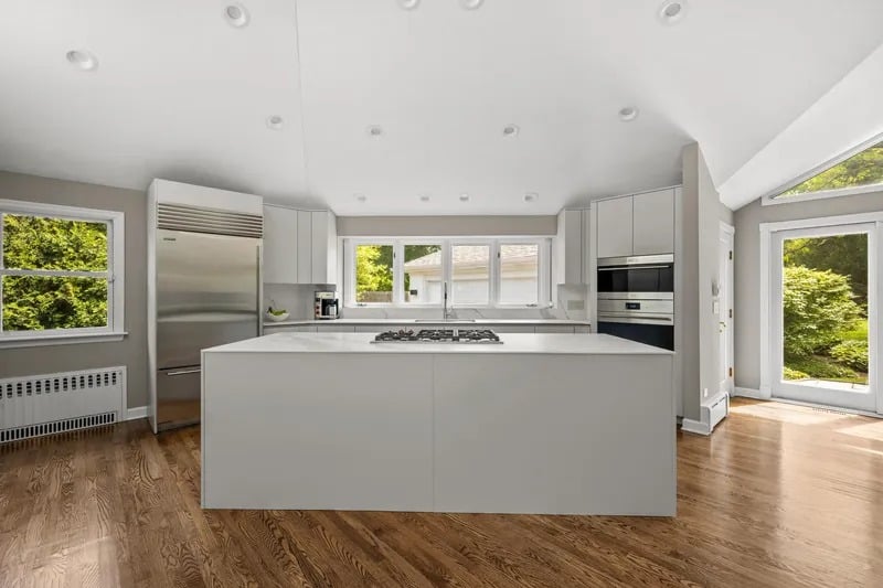 Modern kitchen with a large white island, stainless steel appliances, and hardwood floors.