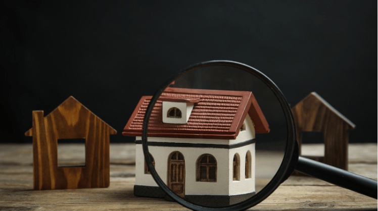 Miniature white house with a red roof viewed through a magnifying glass.