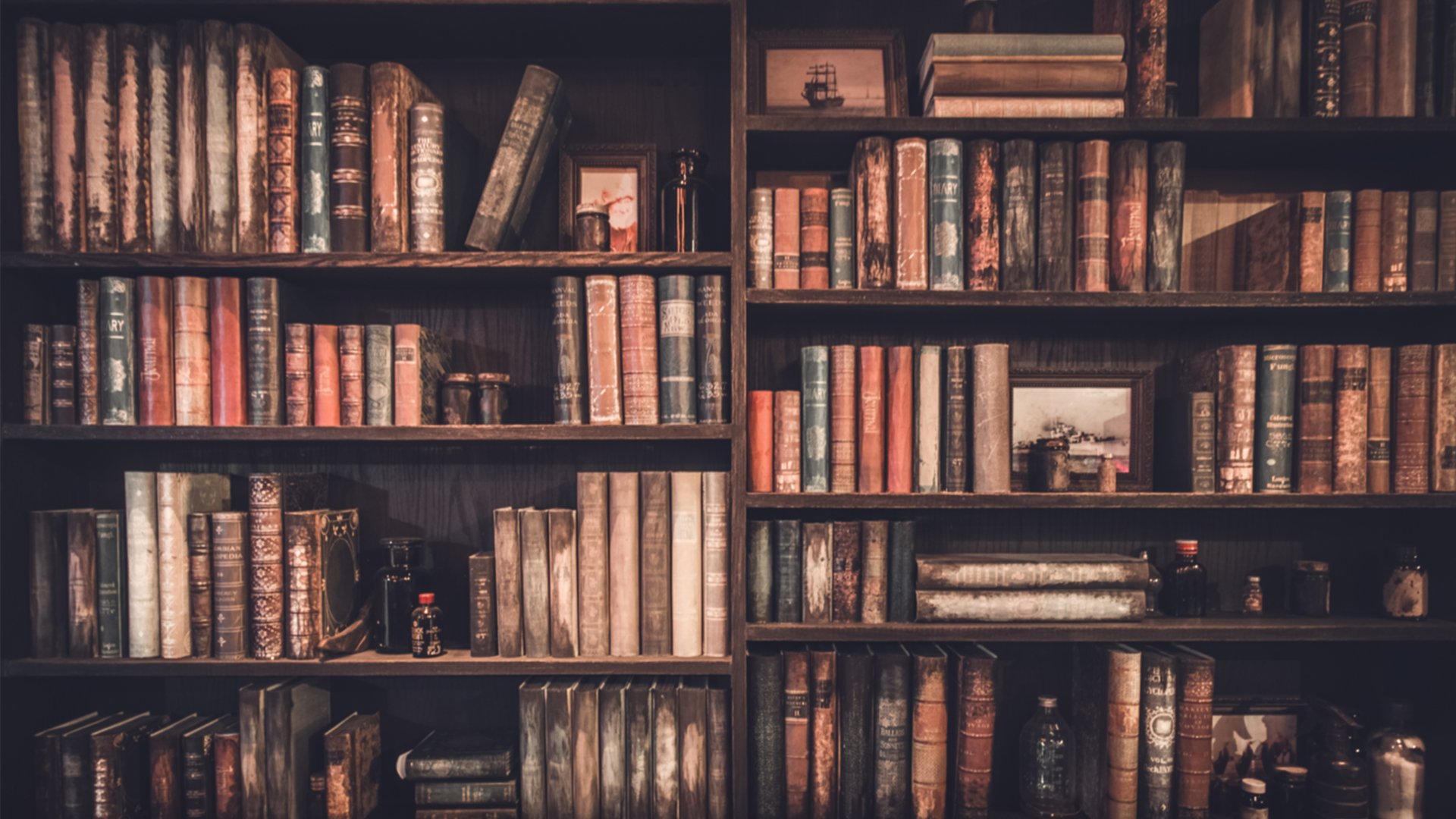 Library shelves filled with antique books and small framed ship pictures.