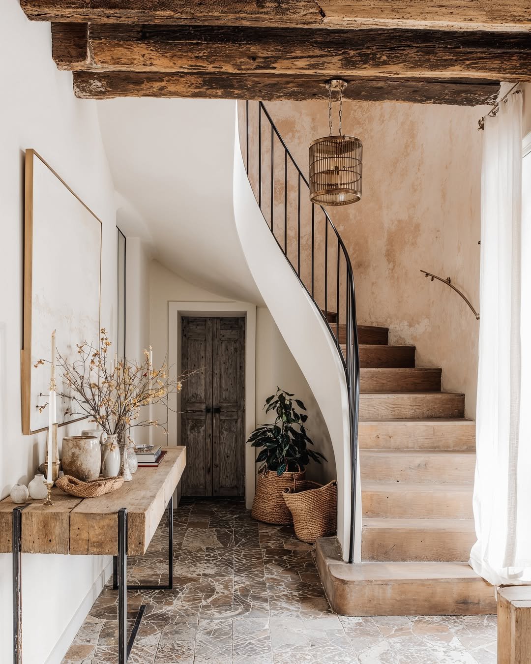 Luxury home interior featuring a curved staircase, natural wood beams, and refined architectural details