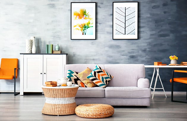 Living room with a pale gray sofa, colorful cushions, woven coffee table, and framed botanical prints.