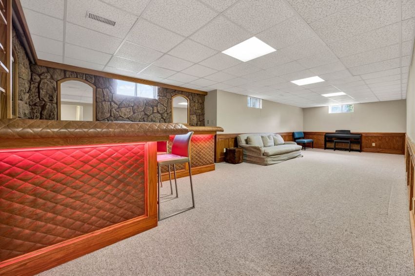 Basement recreation room with a red-fronted bar, stone accent wall, sofa, and piano.