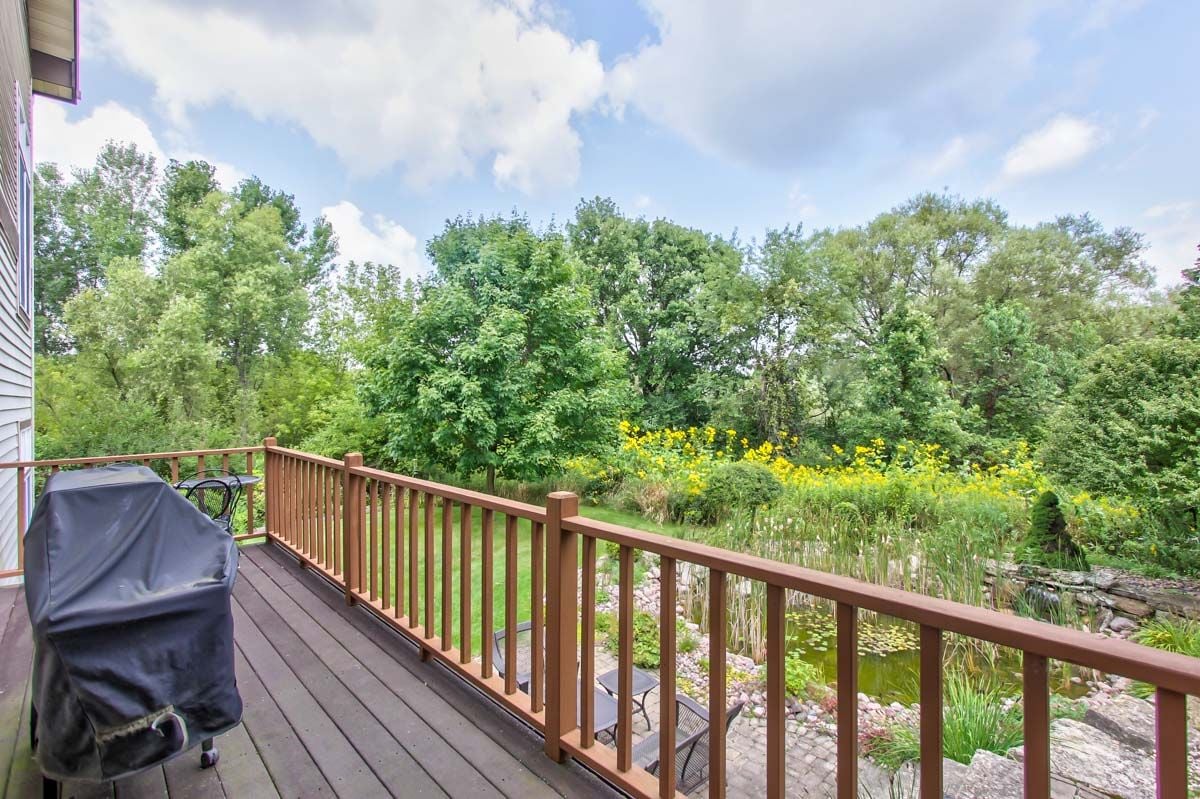 Wooden deck overlooking a pond and garden, with a covered grill and yellow wildflowers.