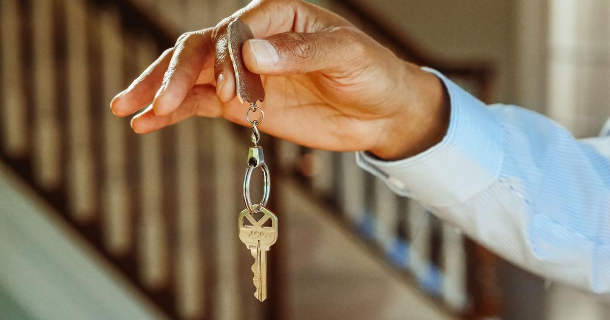 A hand holds a brass house key on a key ring.