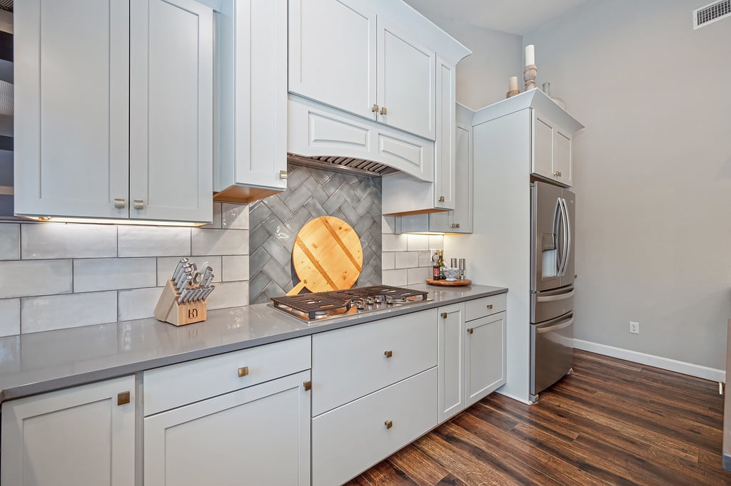 Kitchen with white shaker cabinets, gray tile backsplash, and stainless steel appliances.