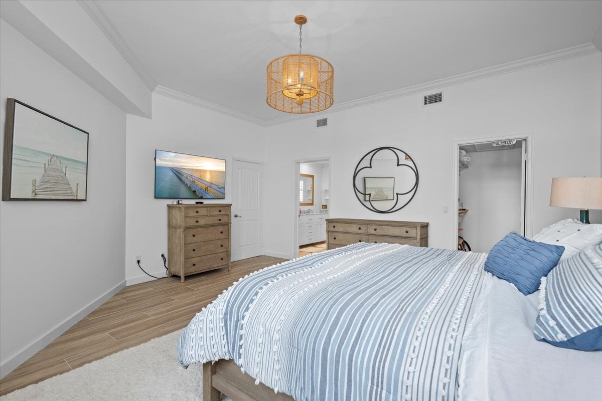 Bedroom with blue-and-white striped bedding, wood dressers, and a woven pendant light.