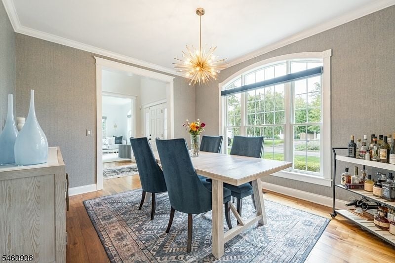 Dining room with a starburst chandelier, dark chairs, and a large arched window.