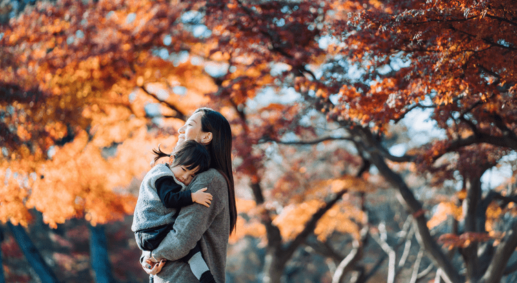 A woman embraces her child amidst vibrant autumn leaves, capturing a moment of warmth and connection in the fall season.