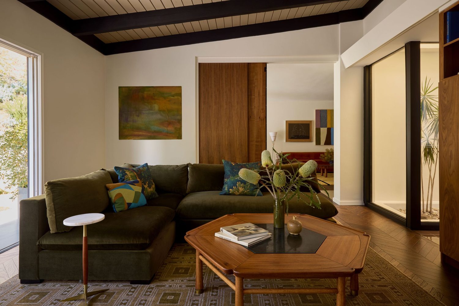 Den with an olive green sectional, walnut paneling, and layered antique art and objects.