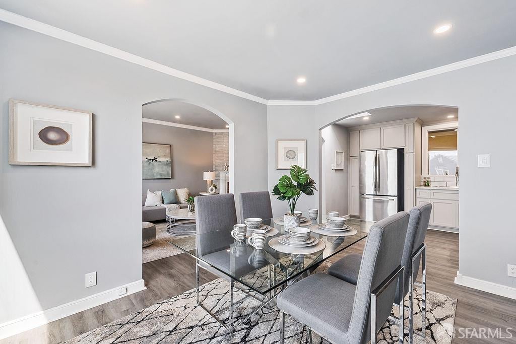Staged dining room with a glass-top table, gray chairs, and arched openings to the living room and kitchen.