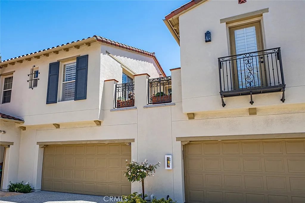 Two-story stucco townhome with wrought-iron balconies, tan garage doors, and a red-tile roof.
