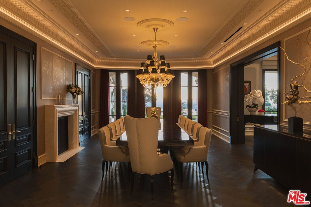 Formal dining room with an ornate chandelier, long table, upholstered chairs, and fireplace.
