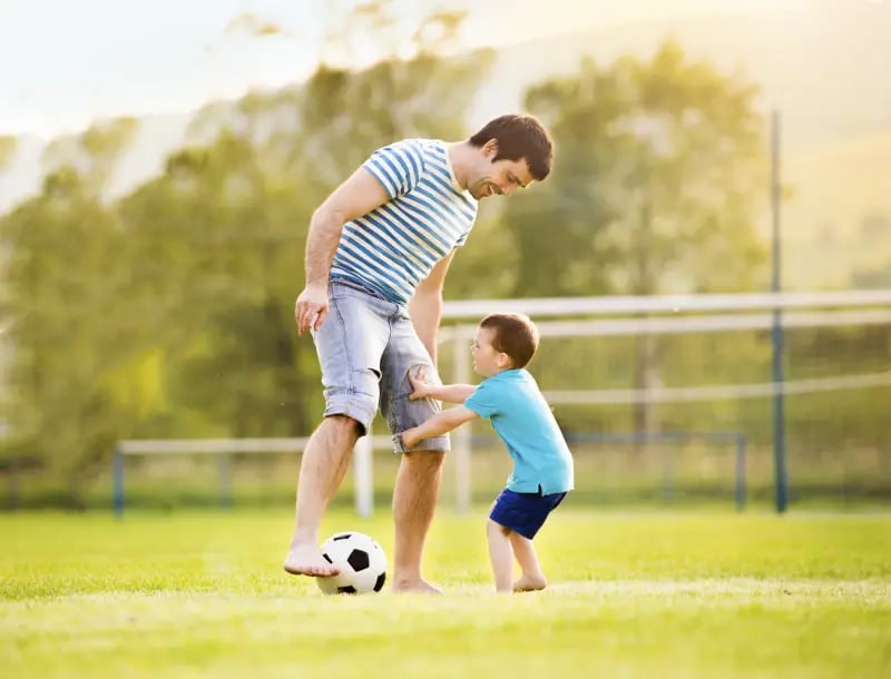 Father and young son playing soccer barefoot on green grass at Aspen park on a sunny day.