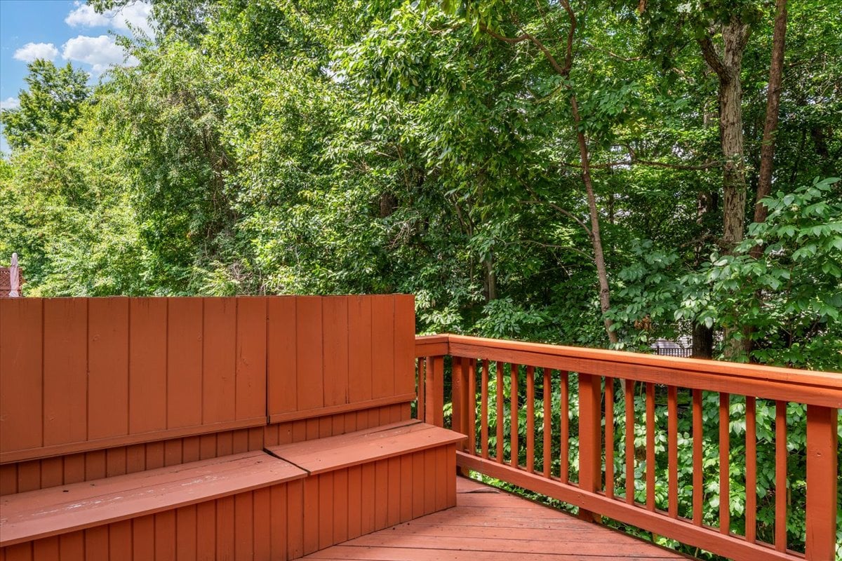 Wooden deck with built-in bench seating overlooking dense green trees.