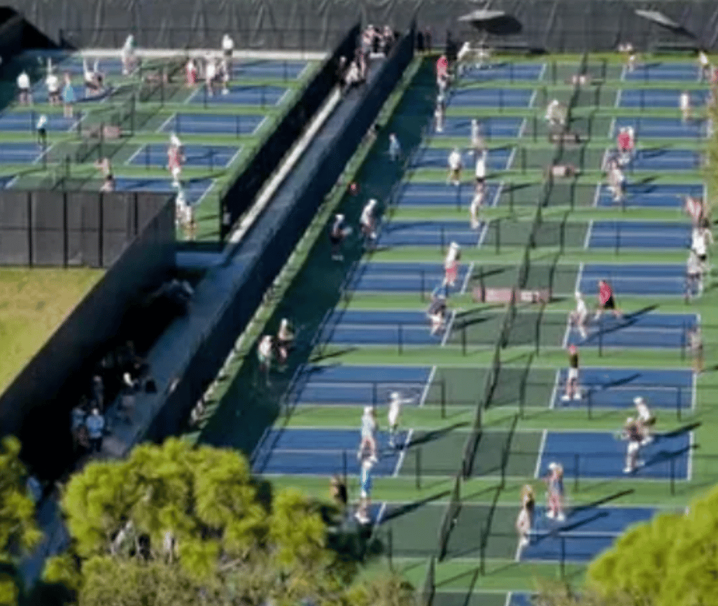 Aerial view of people playing on rows of blue-and-green fenced sports courts.