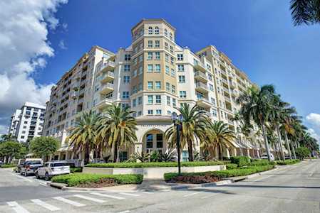 Beige condominium building with balconies, palm trees, and landscaped grounds along the street.