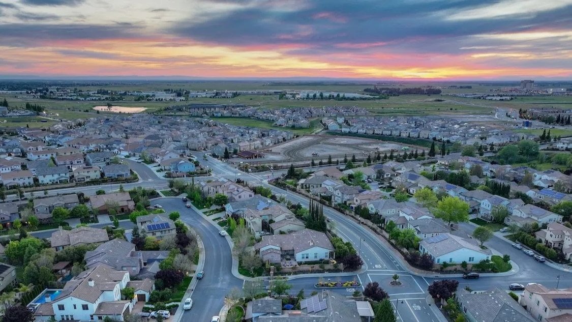 Aerial view of suburban homes and curving streets beneath a colorful sunset.