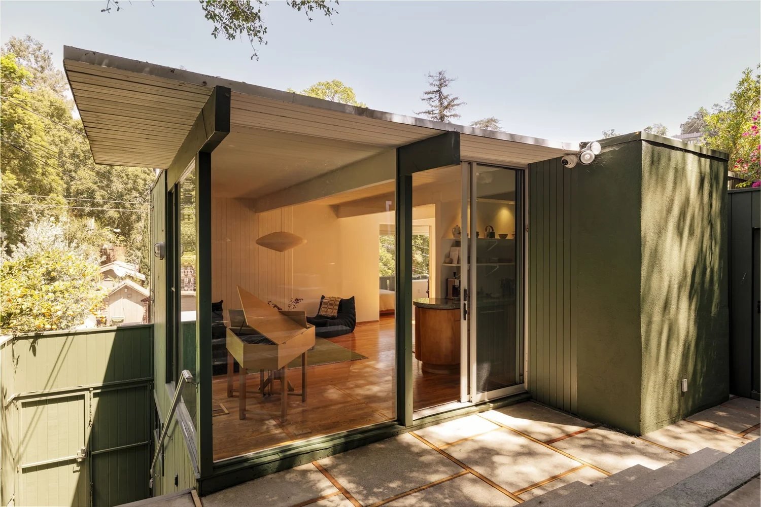 A wall of floor-to-ceiling glass under a thin flat roof opens the living area of the Smith Residence onto a concrete-paved courtyard.