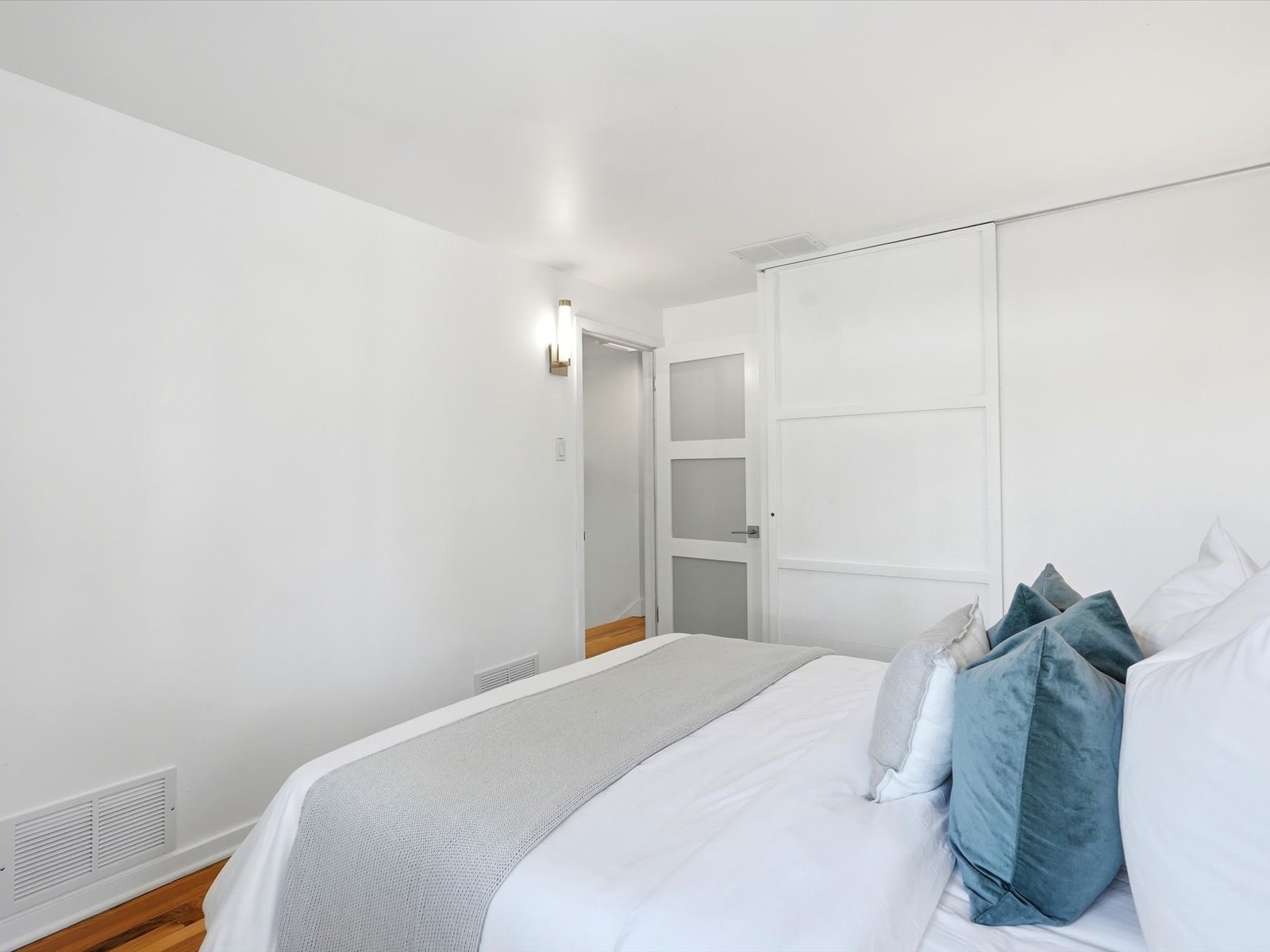 Staged bedroom with a white bed, blue accent pillows, and white paneled sliding doors.