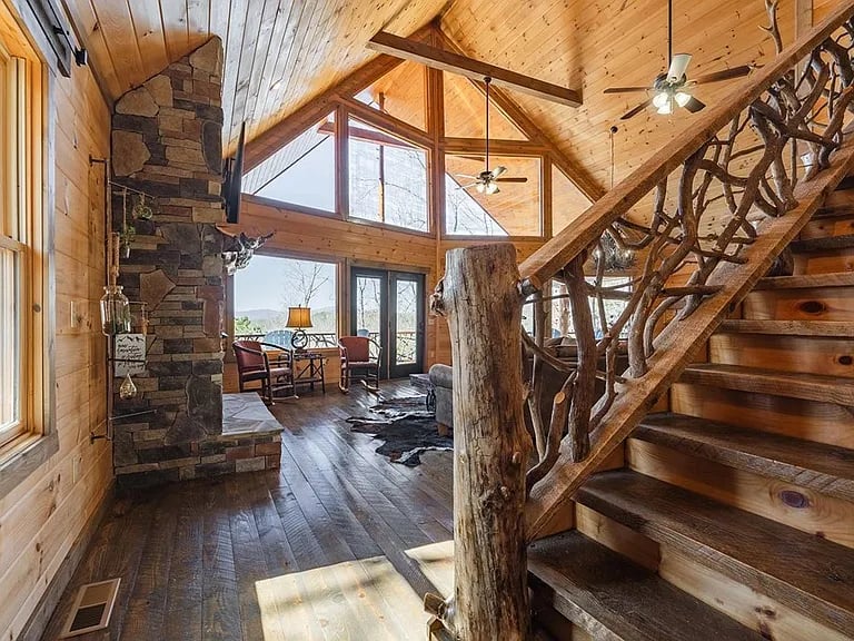 Vaulted wood great room with a stone fireplace and rustic branch staircase.