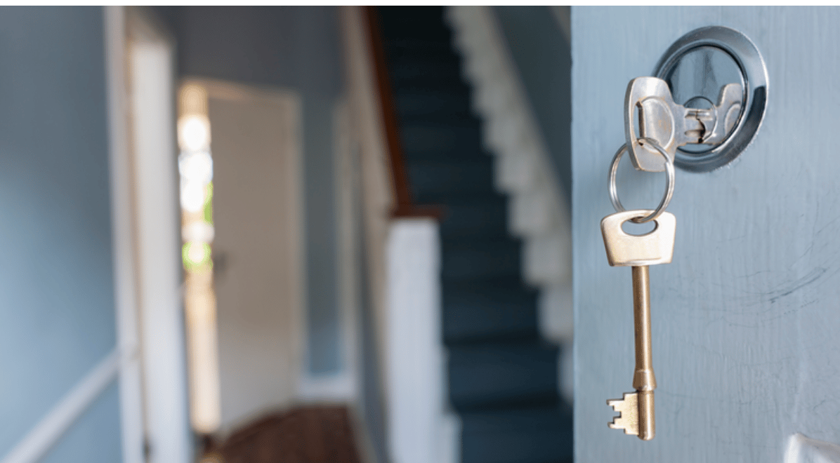 House key hanging from a blue door lock, with a staircase in the background.