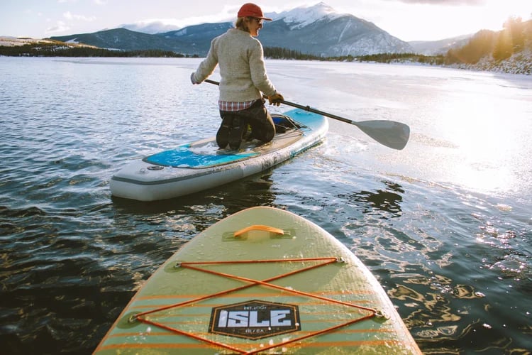 Paddleboarder on a mountain lake with snow-covered peaks in the distance.