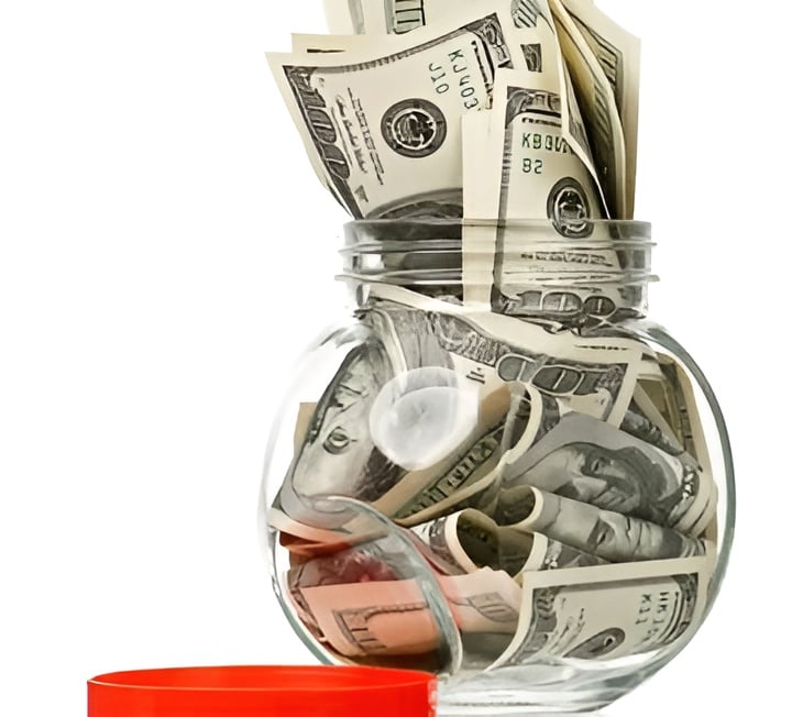 Glass savings jar packed with cash, with dollar bills sticking out of the top.