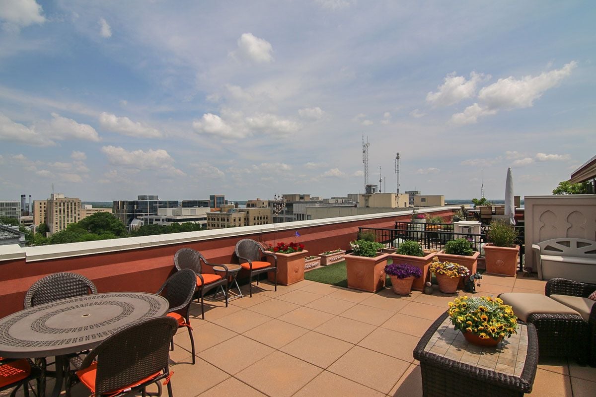 Downtown penthouse rooftop terrace with wicker seating, flower planters, and city views.