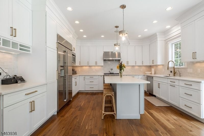 Bright white kitchen with a large island, stainless steel appliances, and warm hardwood floors.