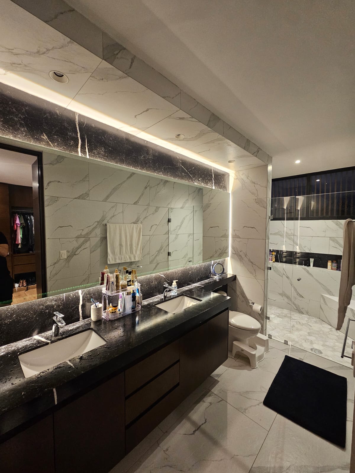 Modern bathroom with a dark double vanity, large mirrors, and a glass-enclosed shower.