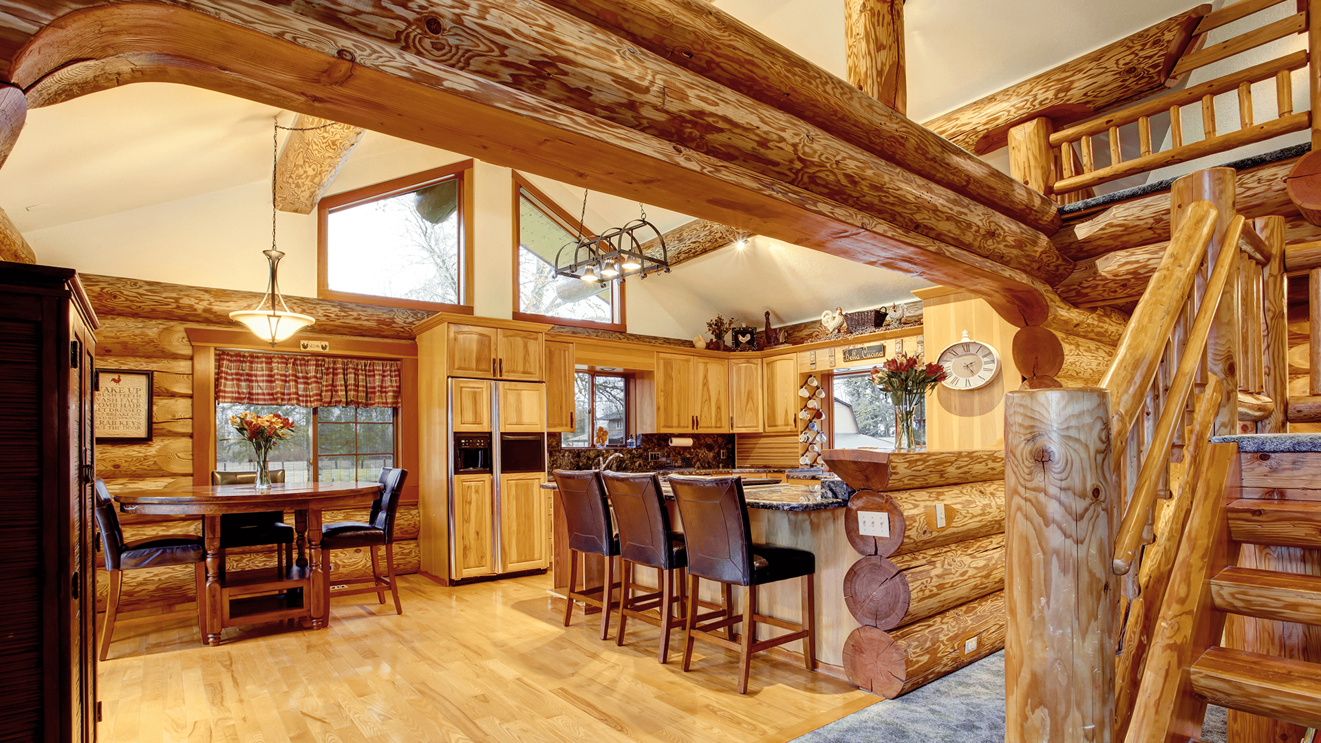 Log-cabin kitchen with a stone island, dining table, exposed beams, and staircase to a loft.