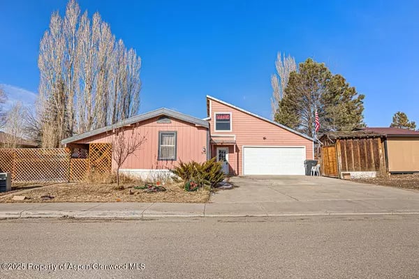 Pink single-story home with an attached white garage, driveway, and fenced side yard.