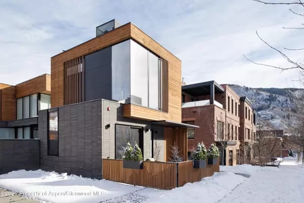 Modern wood-and-stone home on a snowy Aspen street, with mountains in the background.